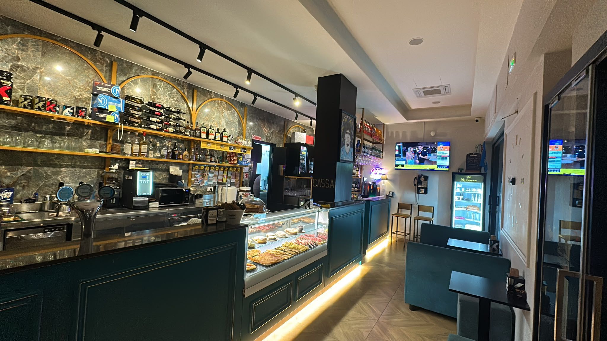 Il bancone del Victory Caffè con gli archi dorati, la vetrina dei dolci e la partita in TV