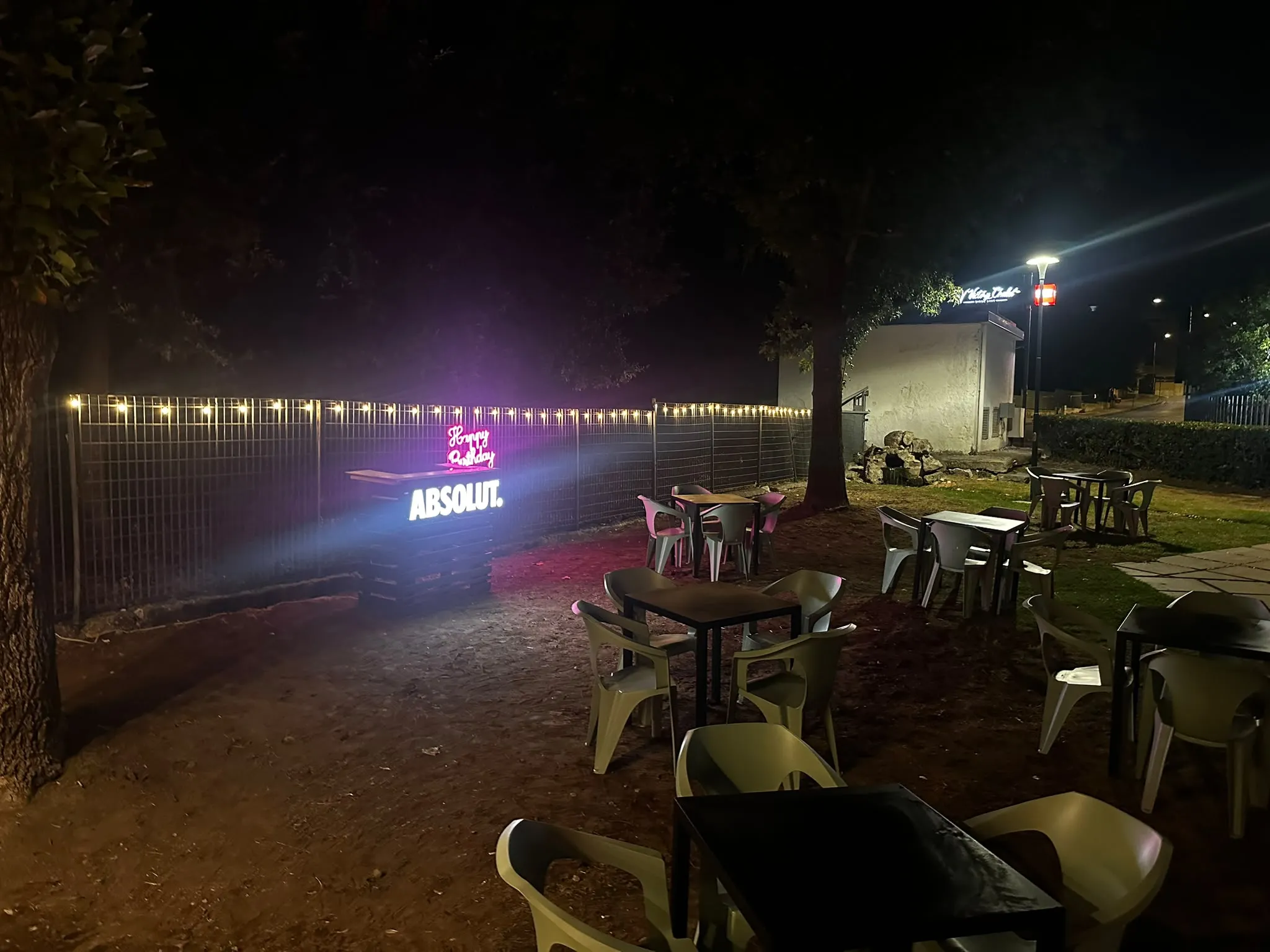 Tavoli sul prato del Victory Chalet di sera, con il bar luminoso e le lucine sulla recinzione